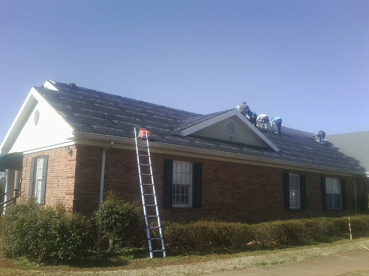 Crew tearing shingles off a brick ranch roof with a ladder set — Emergency Roof Repair work by our crew in Hillburn