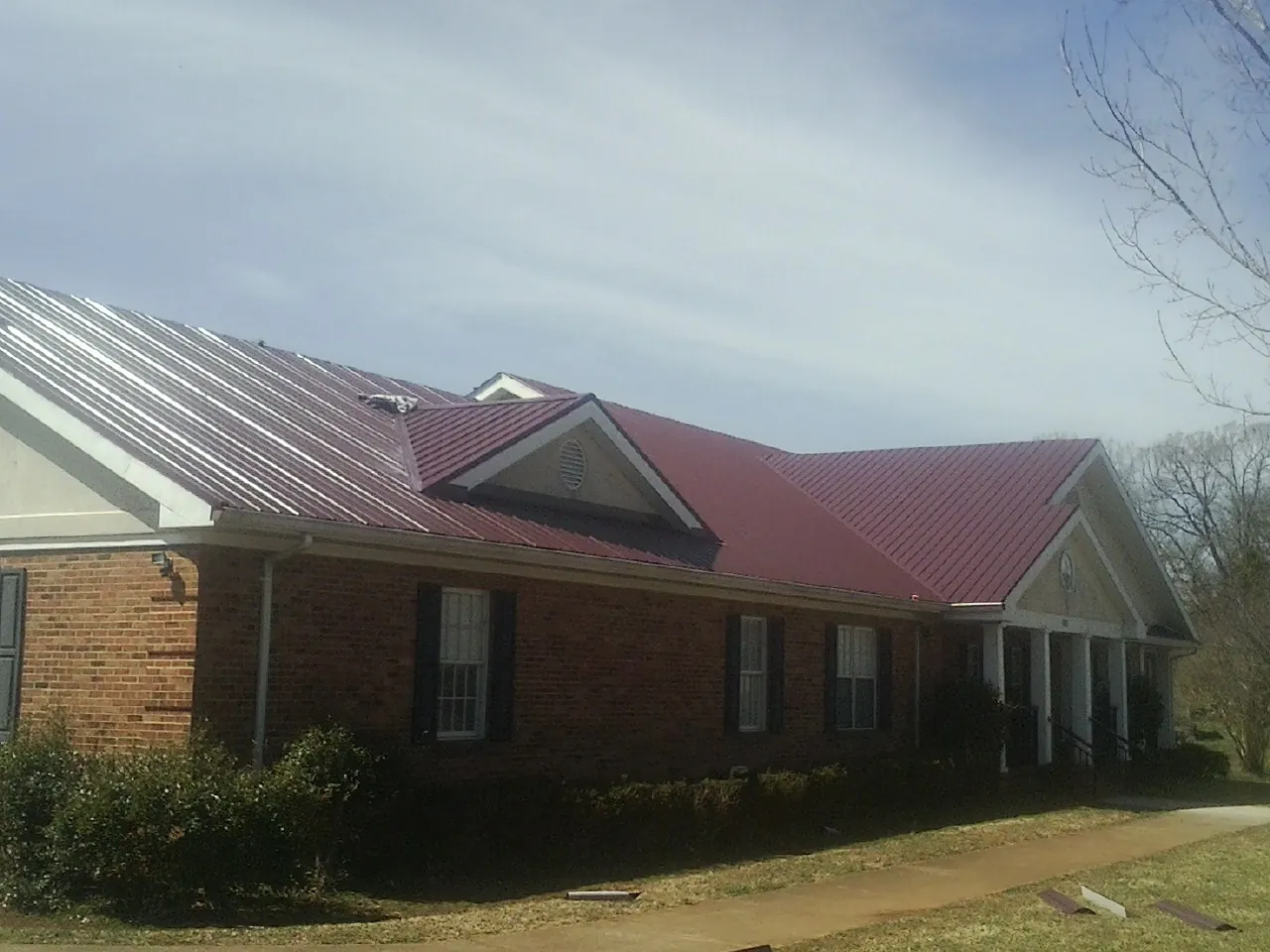 Red metal roof with gabled entries on a long brick building, from a Hail Damage Roof Repair job in Hillburn