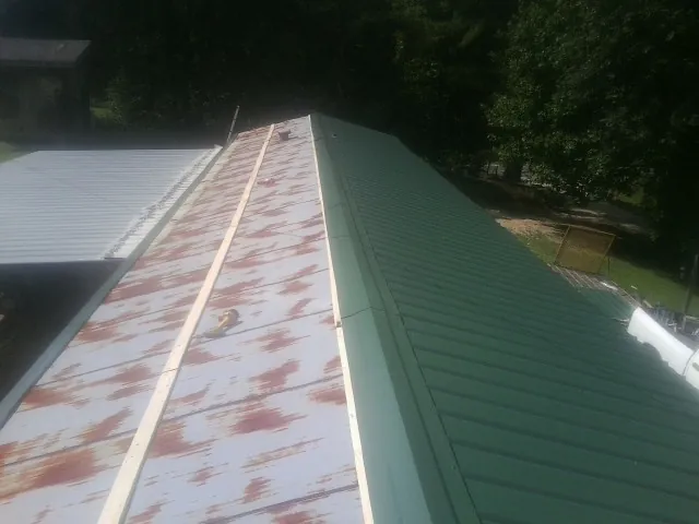 Old rusted panels beside newly installed green metal roofing — Wind Damage Roof Repair by Roofing Brothers in Hillburn