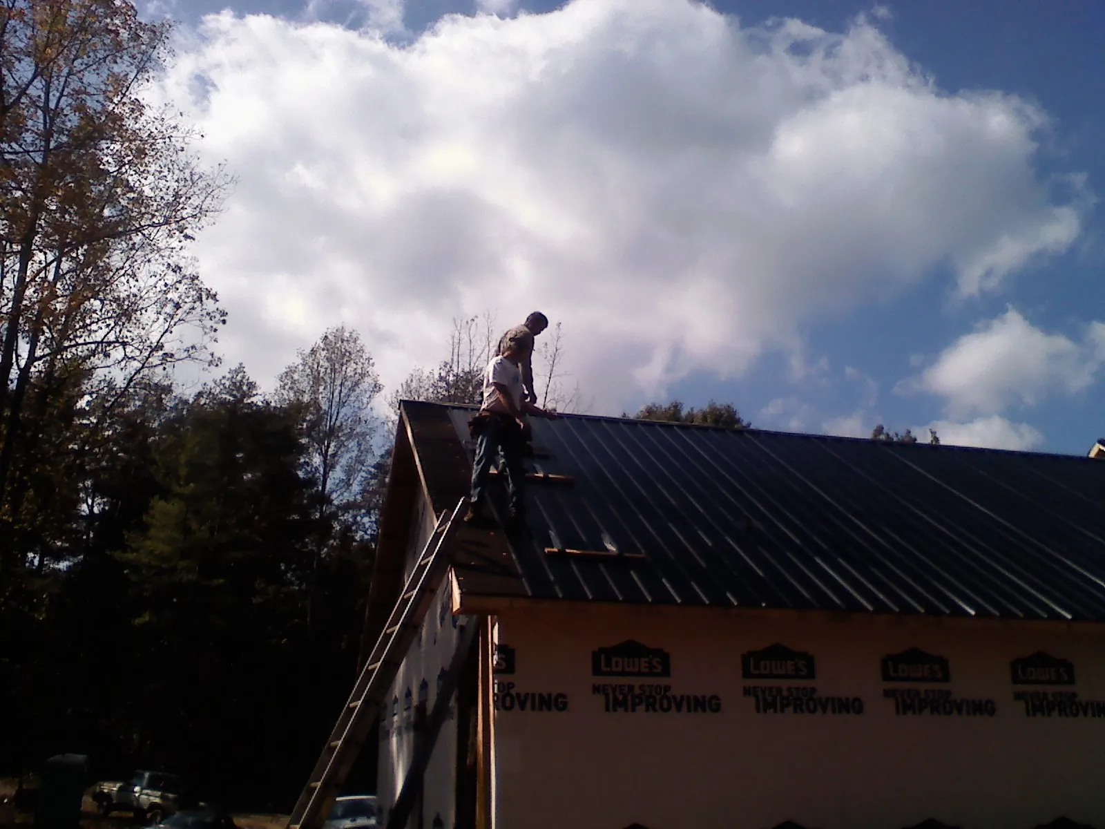 Roofer fastening dark metal panels high against a cloudy sky, from a Roof Inspection job in Hillburn