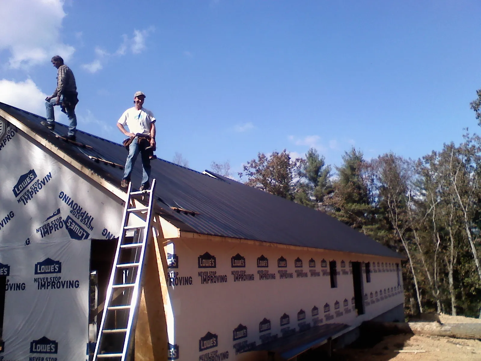Two roofers standing on a long dark metal roof over a wrapped building in Hillburn