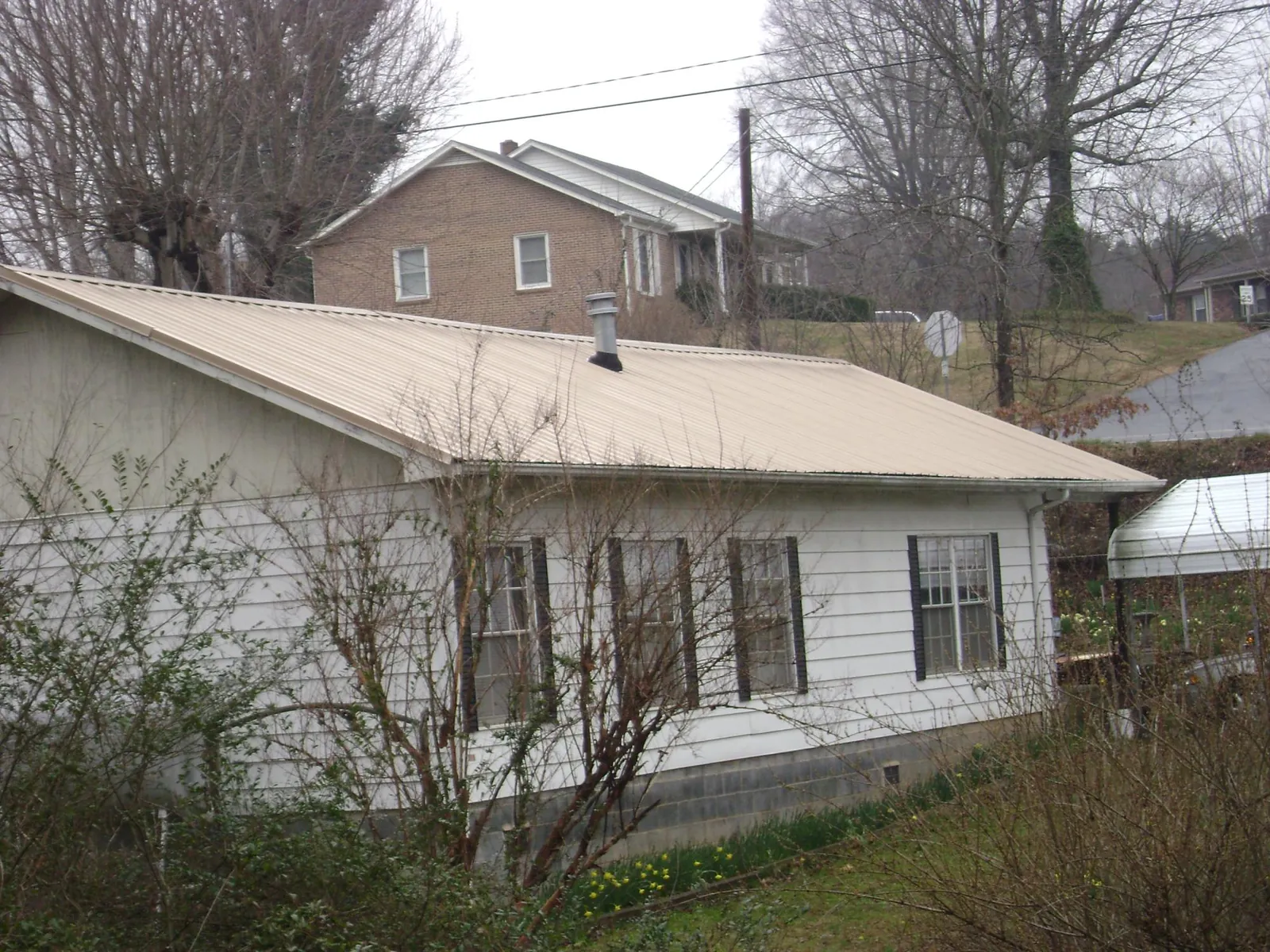 Tan metal roof on a white sided house set into a hillside — Commercial Roofing by Roofing Brothers in Hillburn